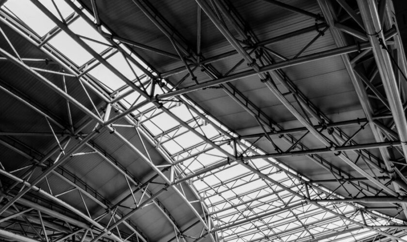 Black and white photo of geometric steel truss ceiling structure, highlighting industrial architecture.