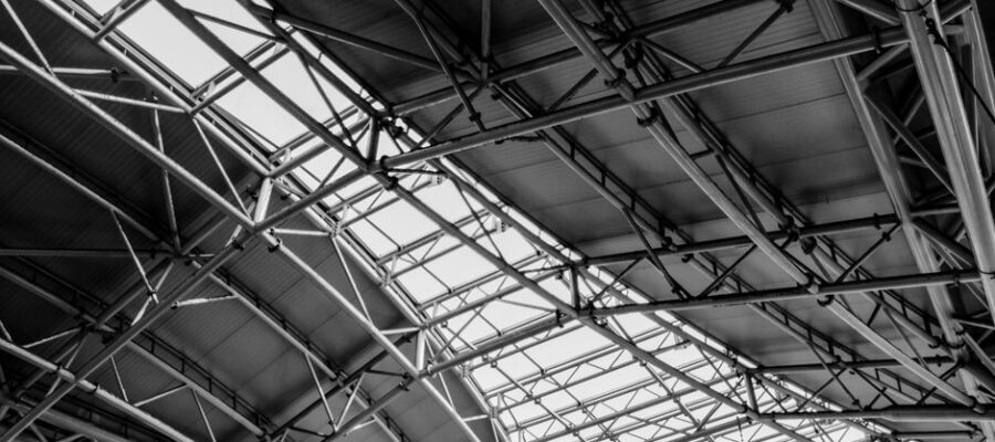 Black and white photo of geometric steel truss ceiling structure, highlighting industrial architecture.