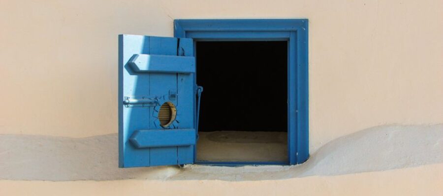 Blue wooden shutter window on a beige wall, open to reveal darkness inside.