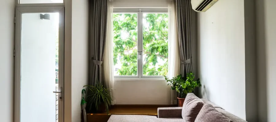 Bright living room with a cozy sofa, indoor plants, and a large window with curtains.