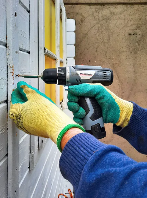 Close-up of a construction worker using a drill on a wooden wall, focusing on hands and tool.