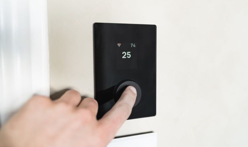Close-up of a hand adjusting a sleek, modern smart thermostat on a wall.