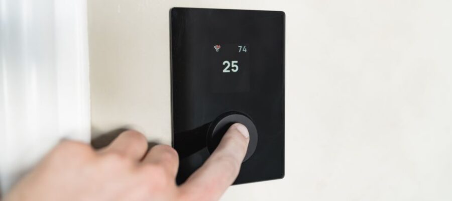 Close-up of a hand adjusting a sleek, modern smart thermostat on a wall.