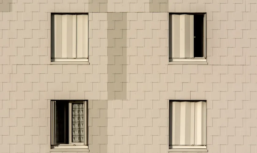 Close-up of a modern apartment building facade with symmetrical windows and beige cladding.