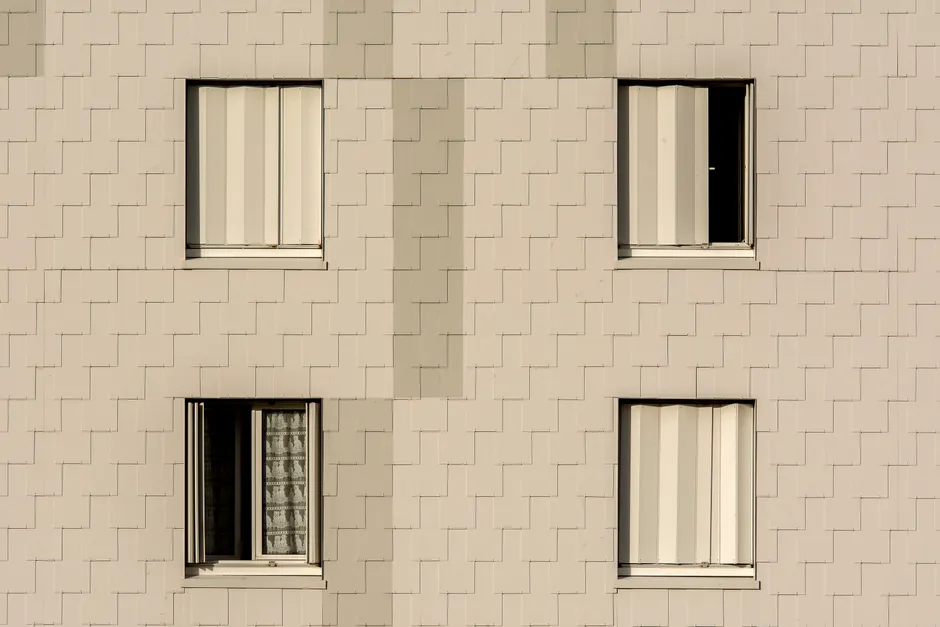 Close-up of a modern apartment building facade with symmetrical windows and beige cladding.