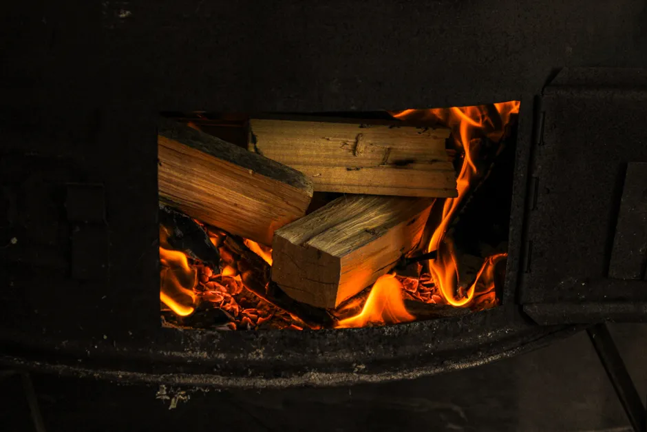 Close-up of firewood burning in a rustic stove, showcasing warm flames and glowing embers.