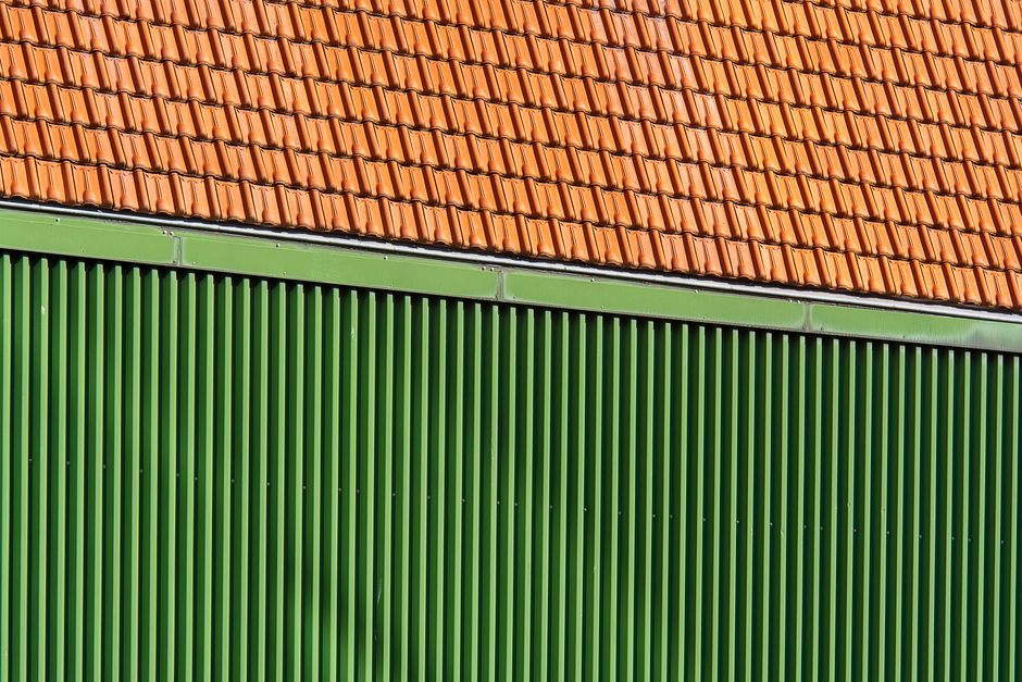 Close-up of vibrant orange roof tiles and green corrugated wall.