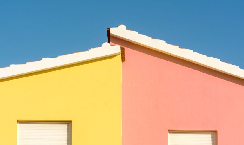 Close-up of vibrant yellow and pink house facades under a clear blue sky.