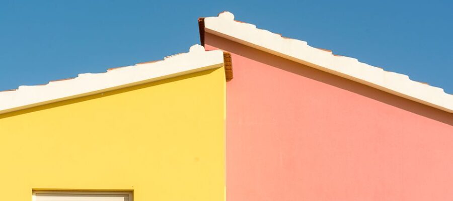 Close-up of vibrant yellow and pink house facades under a clear blue sky.