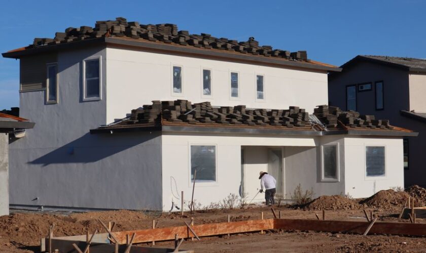Construction site featuring a modern house and a roofer working on roofing tiles.