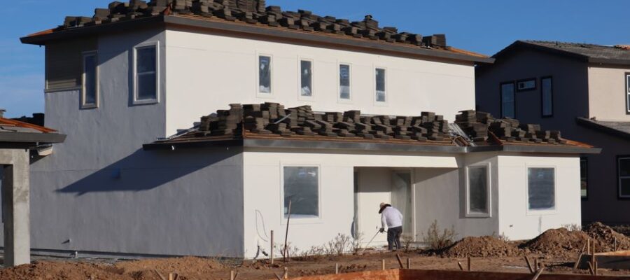 Construction site featuring a modern house and a roofer working on roofing tiles.