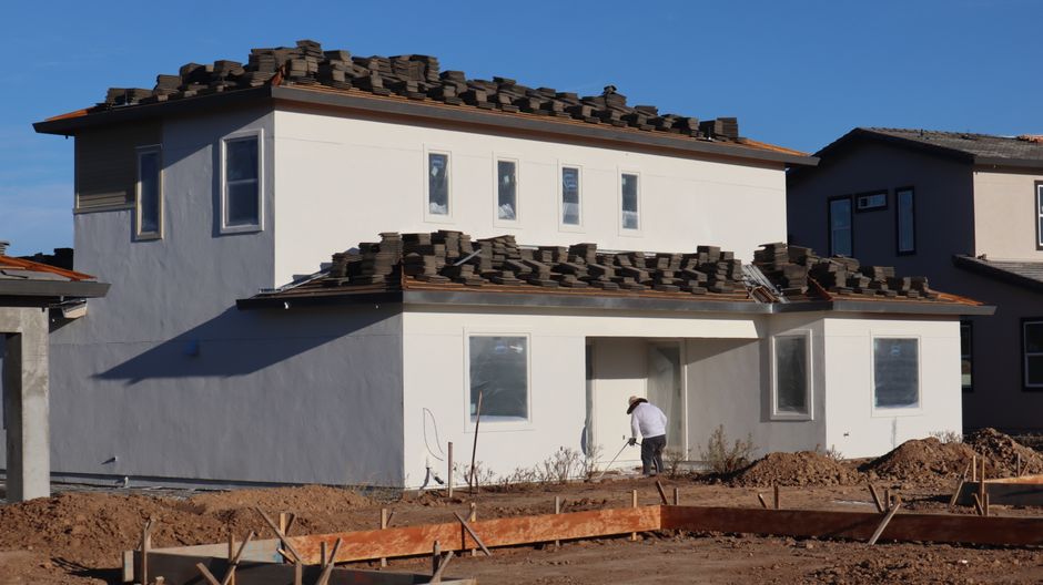Construction site featuring a modern house and a roofer working on roofing tiles.