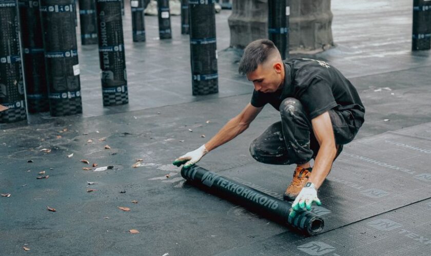 Construction worker applies waterproof membrane on rooftop for protection against weather elements.