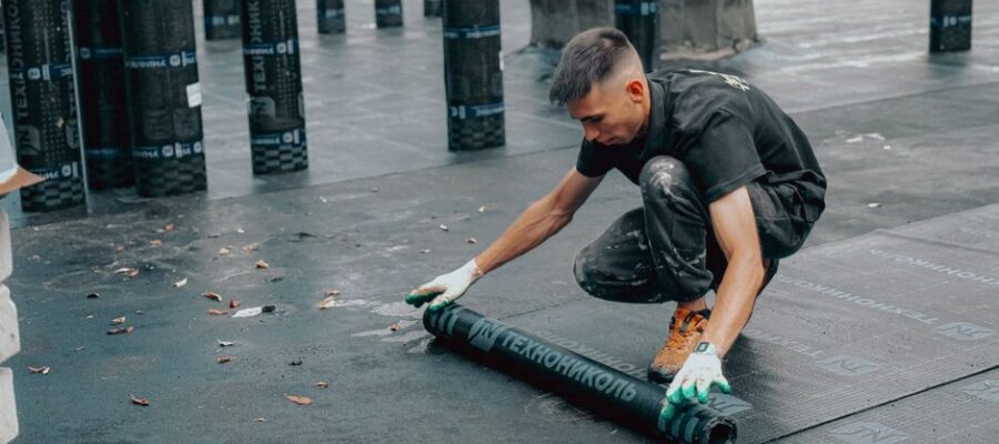 Construction worker applies waterproof membrane on rooftop for protection against weather elements.