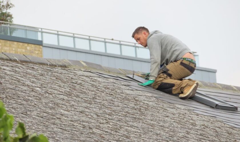 Construction worker installing shingles on a rooftop. Outdoor building maintenance.