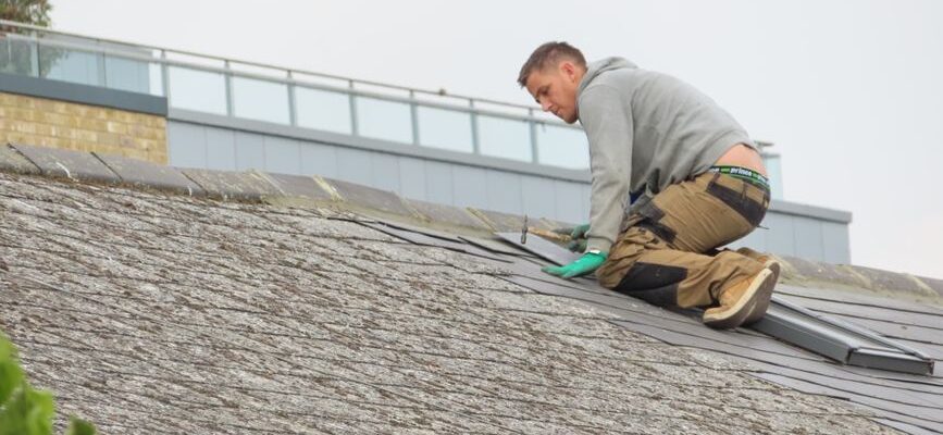 Construction worker installing shingles on a rooftop. Outdoor building maintenance.