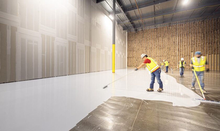 Construction workers in hard hats and vests laying a fresh concrete floor inside a building in Dallas, Texas.