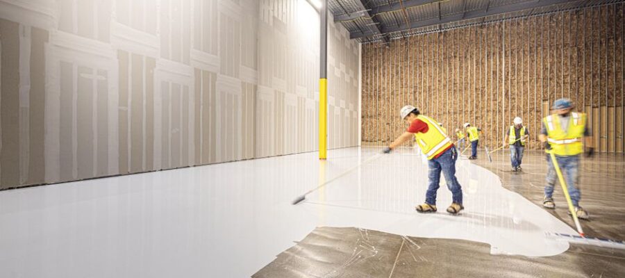 Construction workers in hard hats and vests laying a fresh concrete floor inside a building in Dallas, Texas.