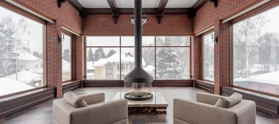 Contemporary living room with armchairs and a central fireplace, snowy view outside.