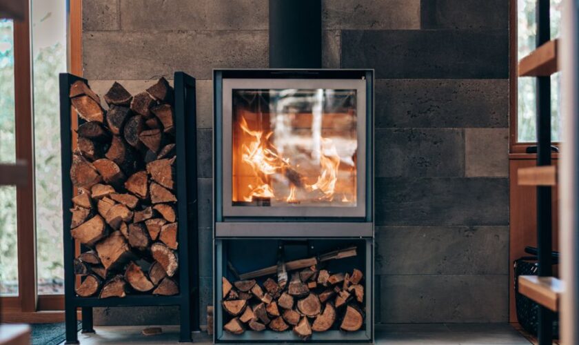 Contemporary square fireplace with burning flame and fuel woods stand located in stylish modern cottage