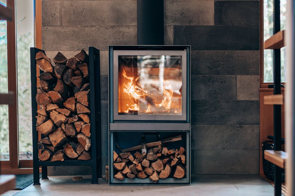 Contemporary square fireplace with burning flame and fuel woods stand located in stylish modern cottage