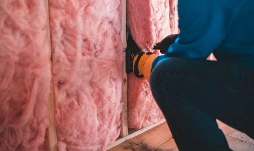 Crop unrecognizable worker in gloves sitting on haunches and insulating with pink stone wool