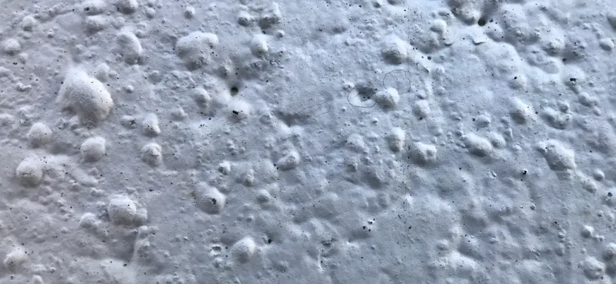 Detailed close-up of a white textured wall with a porous surface in natural light.