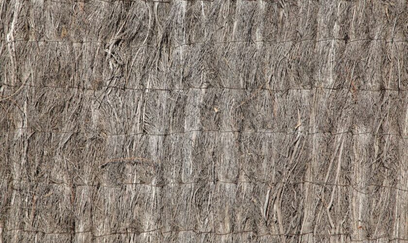 Detailed texture of a natural straw fence with woven fibers and rough surface.