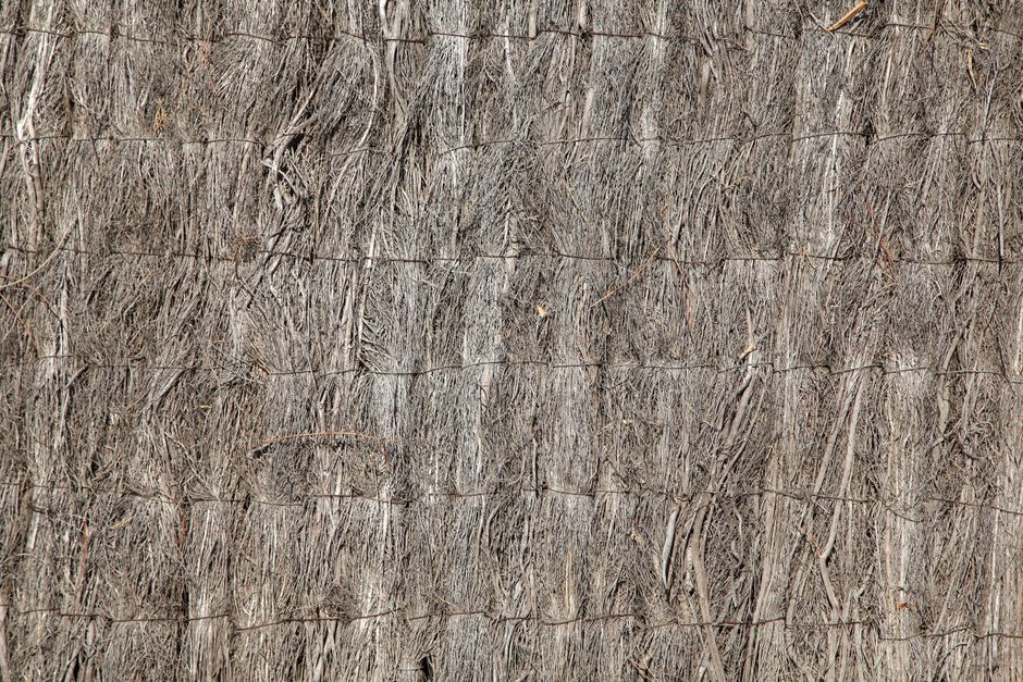 Detailed texture of a natural straw fence with woven fibers and rough surface.