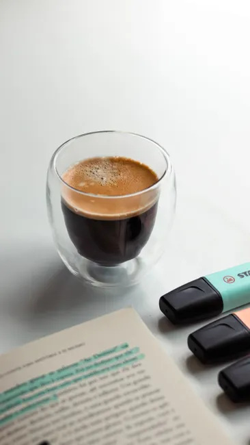 Double-walled espresso glass with highlighters and book on a white background.