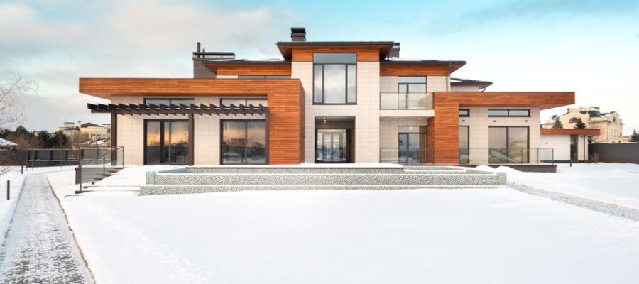 Exterior design of modern cottage house facade with large windows and mixed wooden and stone cladding and spacious yard in snowy winter suburban area