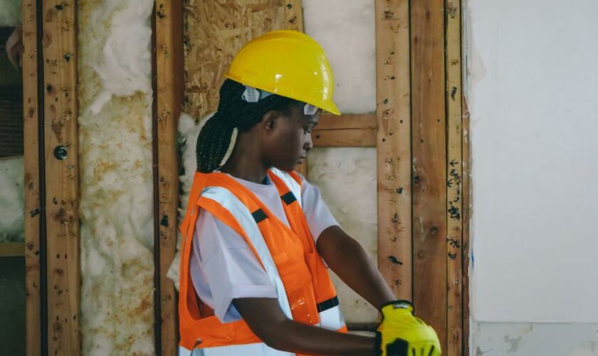 Female construction worker in PPE hammering indoors on a renovation site.