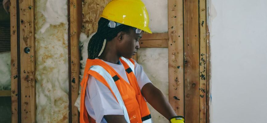 Female construction worker in PPE hammering indoors on a renovation site.