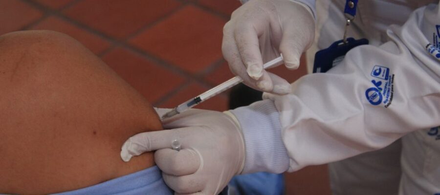 Healthcare worker in protective gear giving a vaccine injection to a patient indoors.