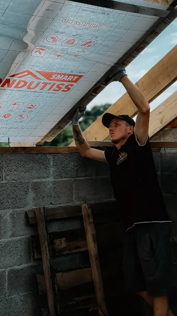 Man working on insulating roof with textile membrane in unfinished construction site. Outdoor building project.