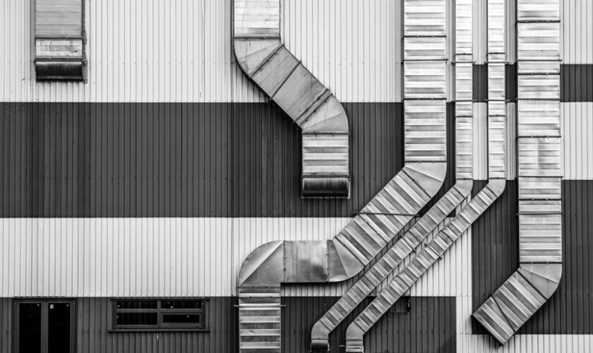 Monochrome image showcasing industrial ductwork and vents on a striped building exterior.