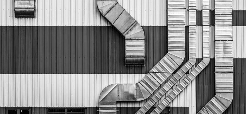 Monochrome image showcasing industrial ductwork and vents on a striped building exterior.