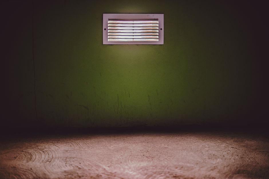 Moody room with a ventilation grate on a textured green wall.