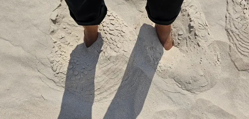 Person with feet buried in sand casting shadows on a sunny beach day.