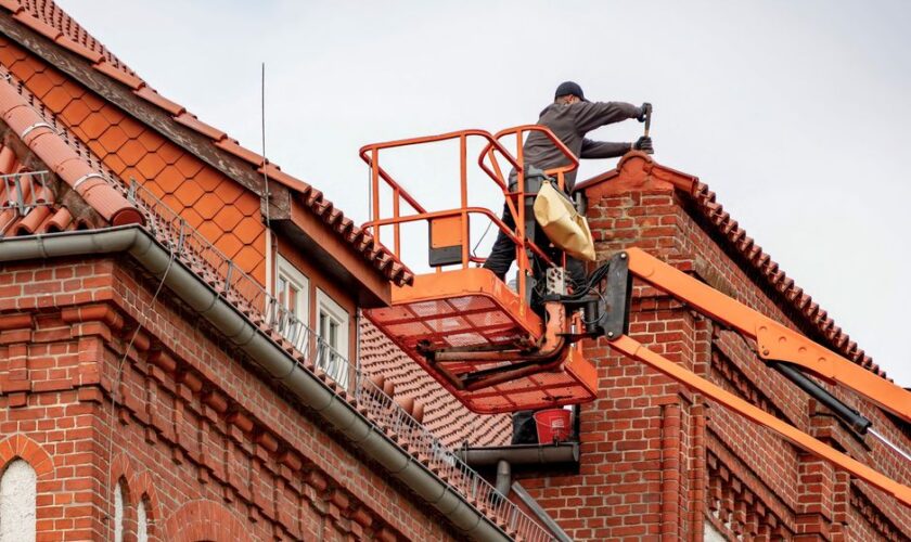Roofer in a cherry picker conducting maintenance on a red brick building with a tiled roof.