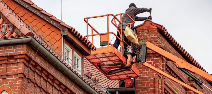 Roofer in a cherry picker conducting maintenance on a red brick building with a tiled roof.