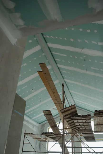 Scaffolding setup in an interior construction space with suspended ceiling boards and wooden planks.