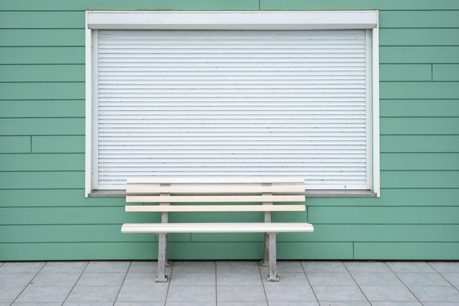 Simple wooden bench by a green wall with closed roller shutter. Ideal for minimalist decor.