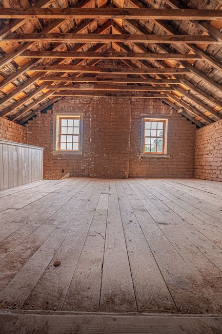 Spacious attic interior featuring exposed wooden beams and brick walls, perfect for renovation or design inspiration.