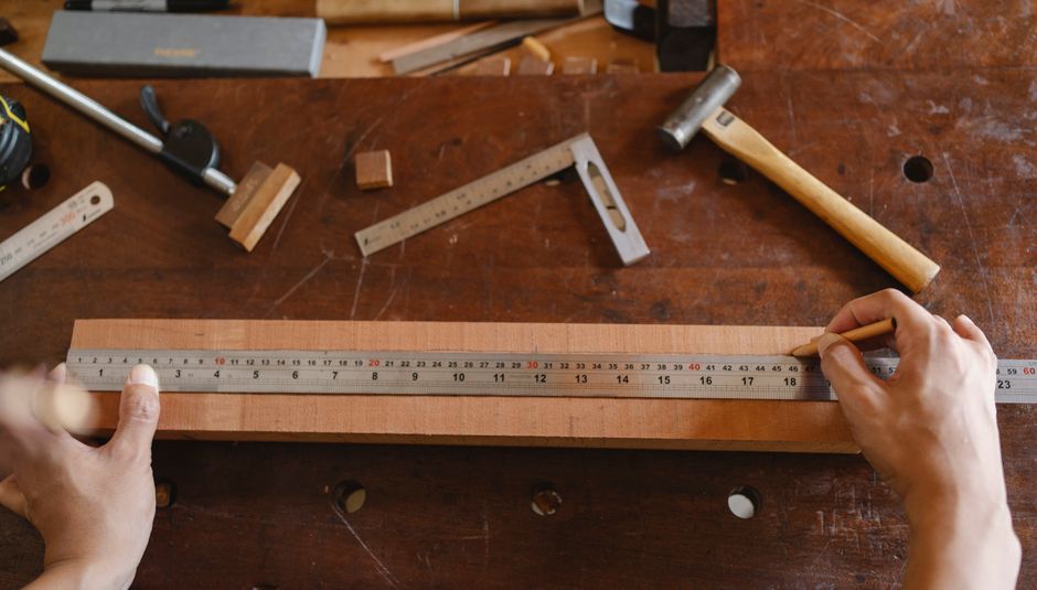 Top view of crop anonymous male using ruler for measuring timber plank on table in workshop