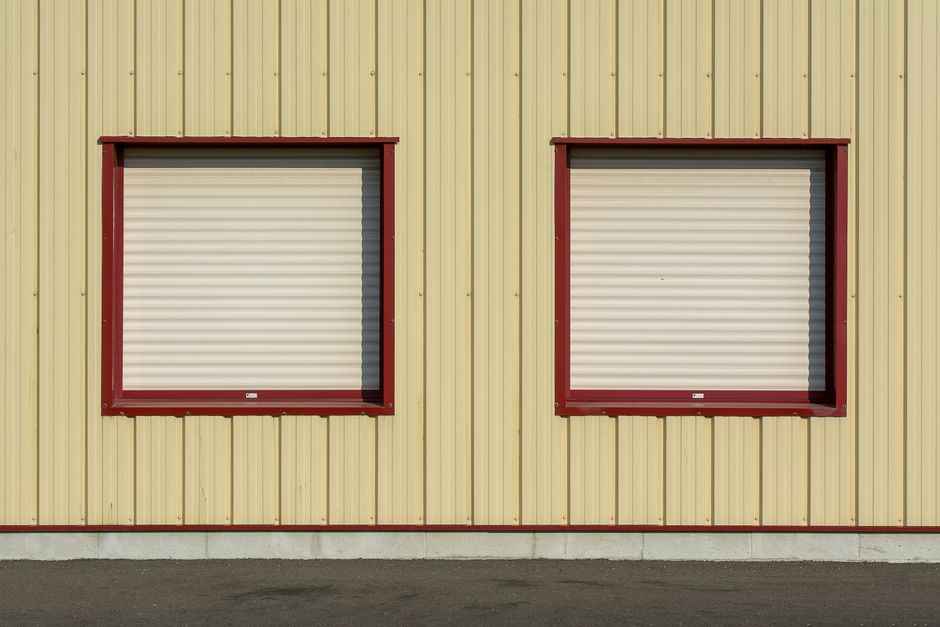 Two closed roller shutters on a yellow industrial building facade, featuring red trim.