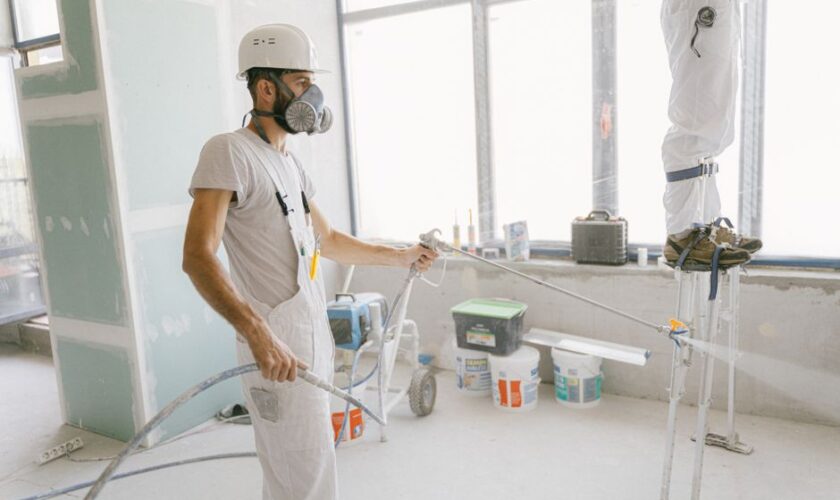 Two construction workers wearing protective gear and painting interior walls for a renovation project.