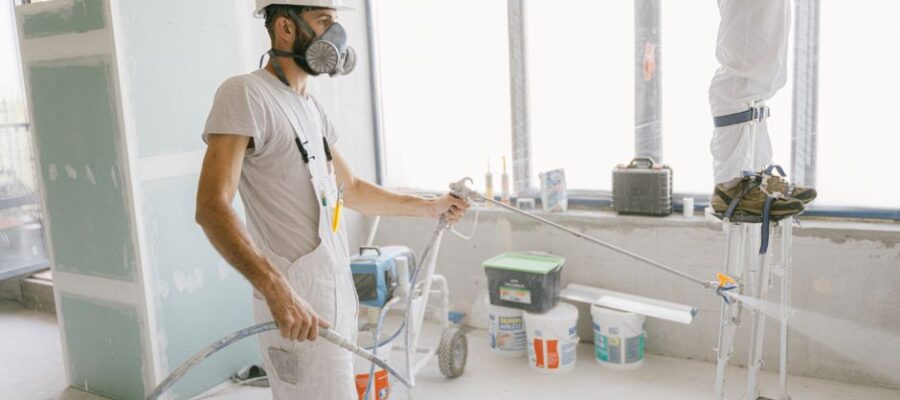 Two construction workers wearing protective gear and painting interior walls for a renovation project.