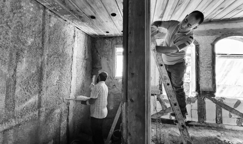 Two men renovating a room, one on a ladder applying plaster, showcasing teamwork and effort.