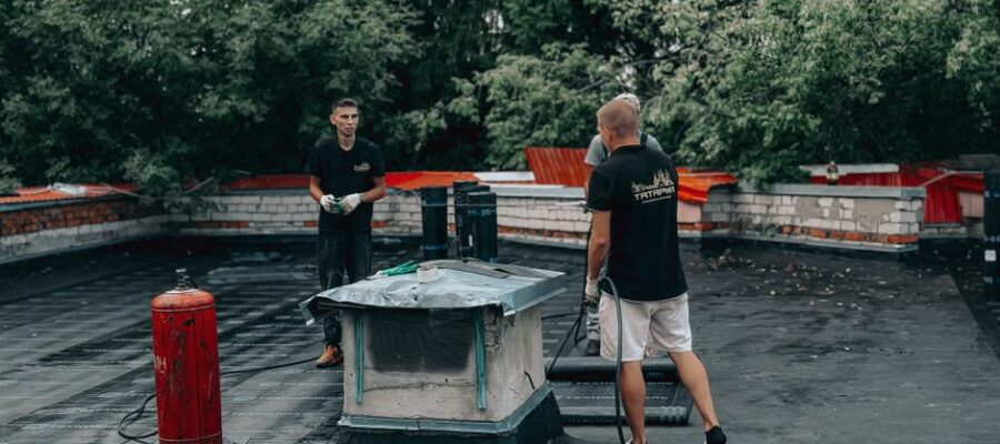 Two workers are performing maintenance on a flat roof with equipment and tools.